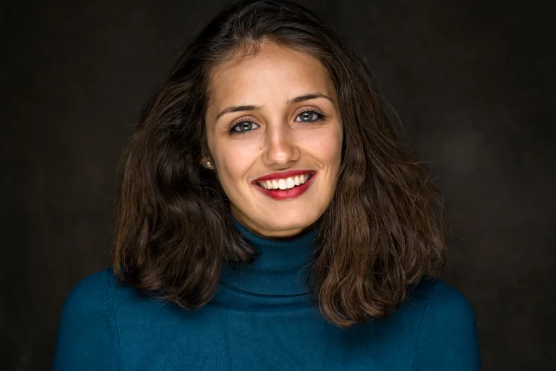 Portrait souriant d’une femme en pull bleu, photographiée sur fond sombre.